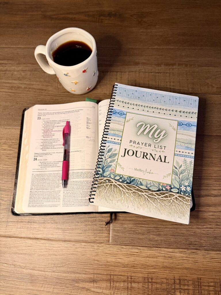 Prayer journal beside an open Bible, pen, and coffee